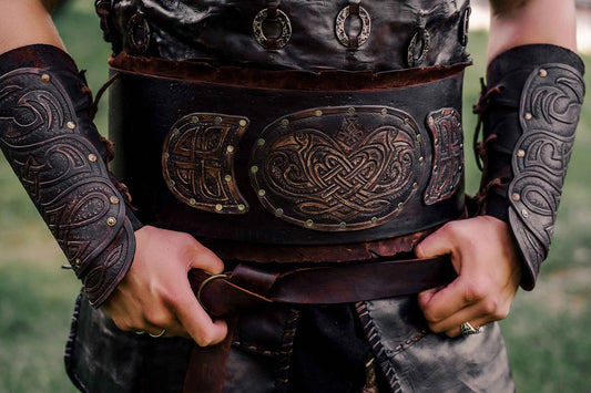 Close view of a wide dark leather warrior belt with carved panels, metal accents, and matching bracers