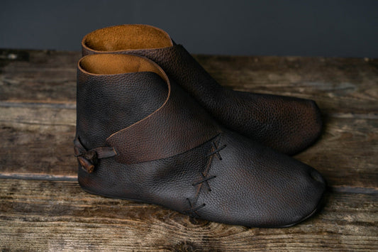 Pair of dark brown ankle-high Viking shoes with wraparound leather panels on a wooden surface