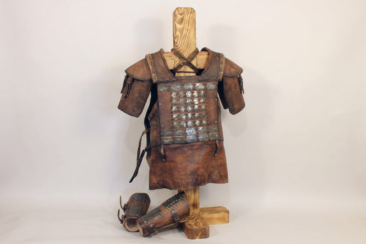 Front three-quarter view of aged brown leather LARP cuirass, pauldrons, and bracers on a wooden stand
