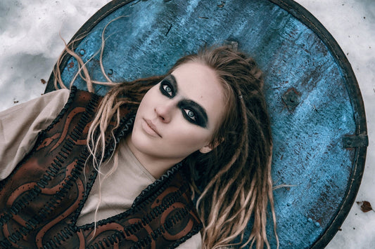 Close portrait of a shieldmaiden character in brown leather armor beside a weathered blue round shield
