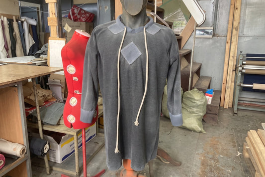 Front view of a gray-blue medieval tunic with long sleeves, rope ties, and contrasting shoulder patches on a workshop mannequin