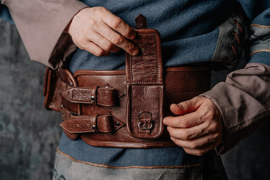 Close view of a brown leather fantasy belt with buckled pouches worn over a blue tunic